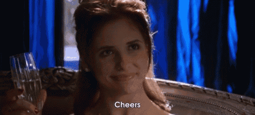 a woman is smiling while holding a glass of wine and the word cheers is on her face .
