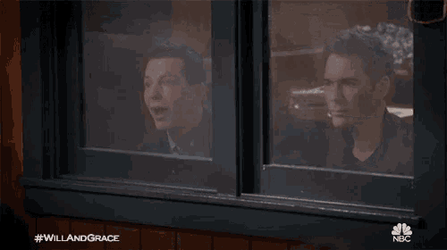a man is laughing while looking out a window with #willandgrace on the bottom
