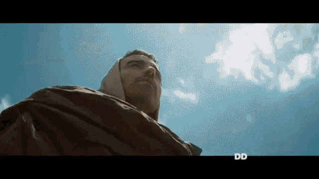 a man in a hooded jacket looks up at a blue sky