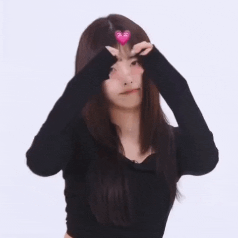 a girl with long hair is making a heart shape with her hands on her forehead .