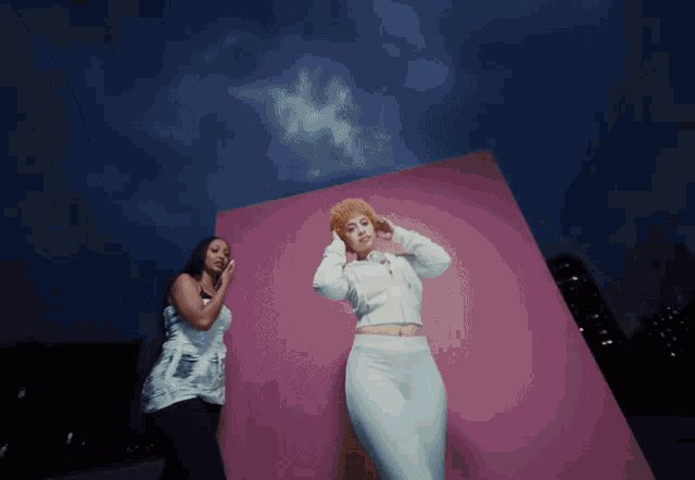 two women standing in front of a pink wall
