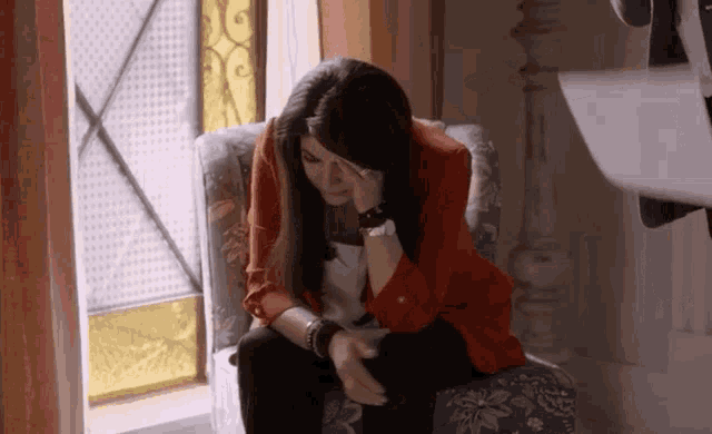 a woman in a red jacket sits in a chair covering her face