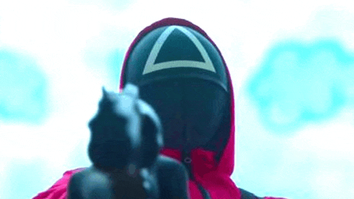 a person wearing a triangle mask is holding a gun in front of their face .