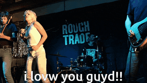 a woman singing in front of a sign that says " rough trade "