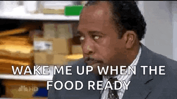 a man in a suit and tie is saying `` wake me up when the food ready '' while sitting at a table .