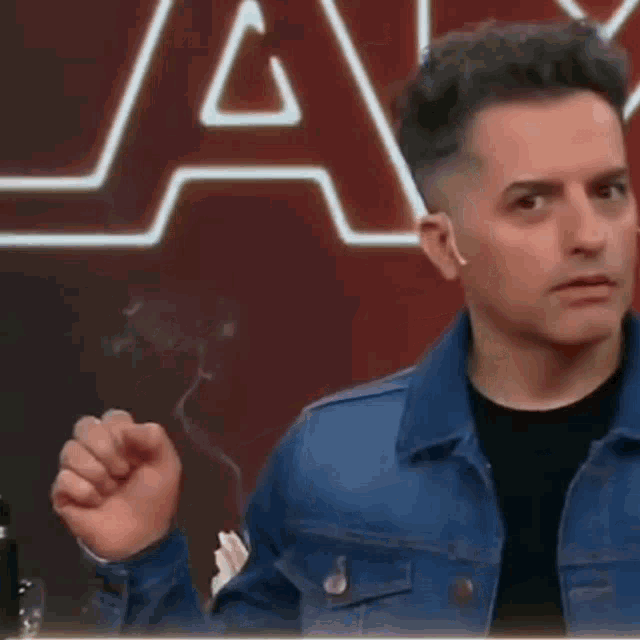 a man in a denim jacket is smoking a cigarette in front of a star wars logo .