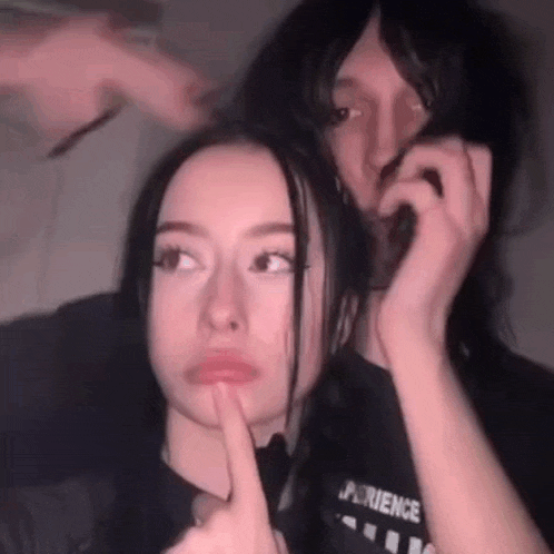 a man and a woman are sitting next to each other and the woman is holding the man 's hair in her hand .