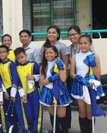 a group of children in marching uniforms are posing for a picture with their teacher .