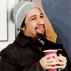 a man wearing a beanie is holding a cup of coffee .