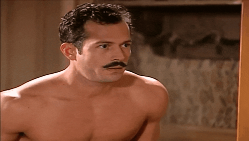 a shirtless man with a mustache stands in front of a door