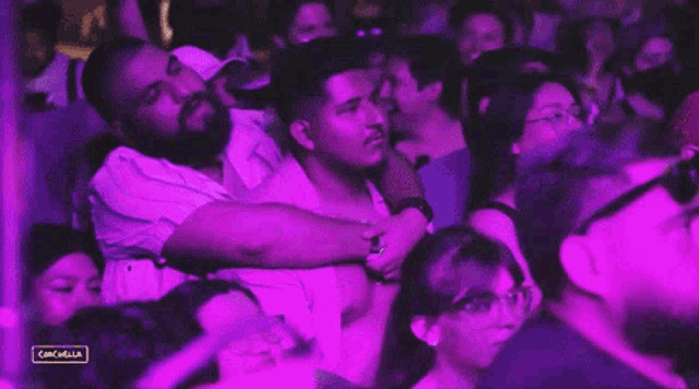a man is hugging another man in a crowd of people at a concert with purple lights .
