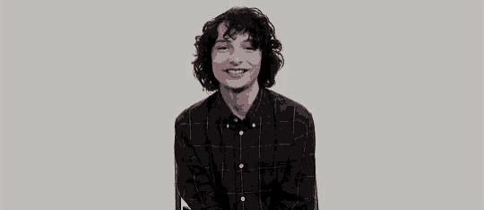 a young man with curly hair is wearing a plaid shirt and smiling while sitting down .