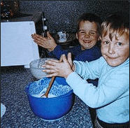 two young boys are mixing ingredients in a blue bowl on a kitchen counter