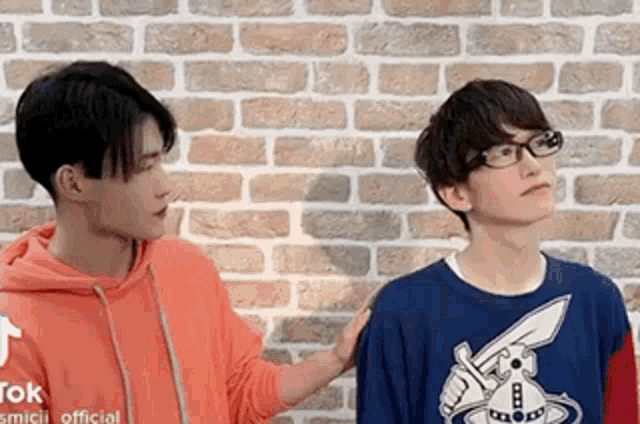 two young men are standing next to each other in front of a brick wall