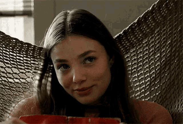 a young woman is sitting in a hammock holding a red cup .