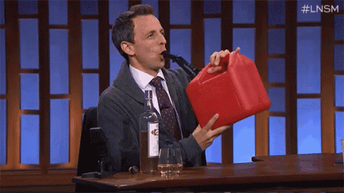 a man is sitting at a table drinking from a gas can .