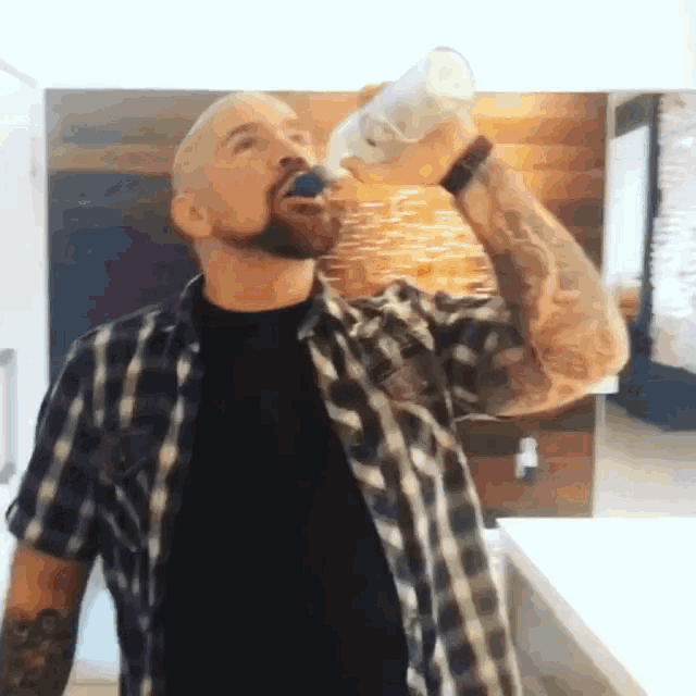 a man in a plaid shirt is drinking water from a clear bottle