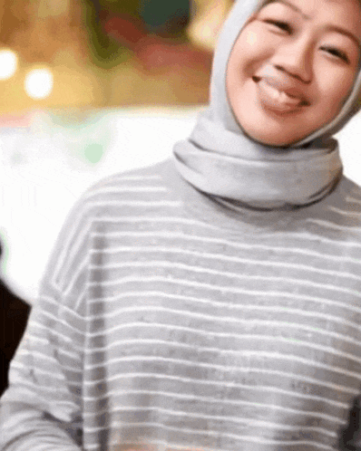 a woman wearing a striped shirt and a hijab smiles for the camera