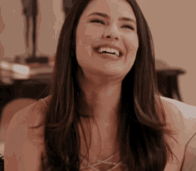 a woman with long dark hair is laughing with her eyes closed .