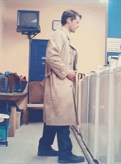 a man in a trench coat is standing in front of a washing machine