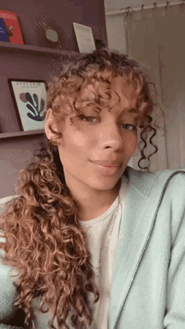 a woman with curly hair is wearing a blue jacket and a white shirt