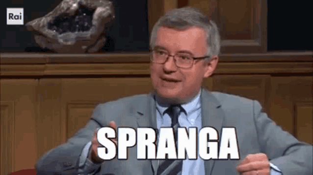 a man in a suit and tie is sitting in front of a statue and says spranga .