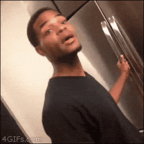 a man in a black shirt is standing in front of a refrigerator with his mouth open