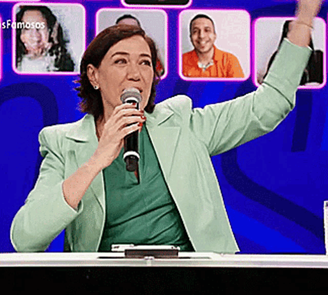 a woman in a green jacket is holding a microphone and raising her hand