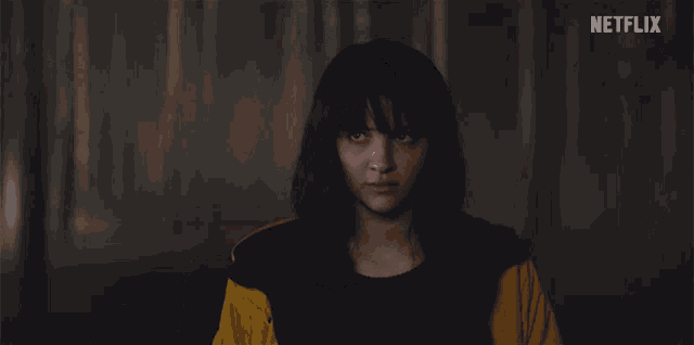 a girl in a yellow jacket looks at the camera with a netflix logo in the background