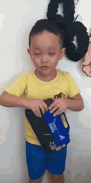 a young boy wearing a yellow shirt and blue shorts is holding a blue and black item .