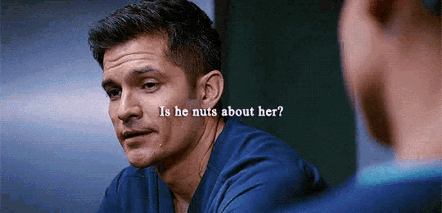 a man in a blue scrub is talking to another man and the words is he nuts about her are written on his face .