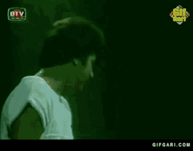 a man in a white shirt is standing in a dark room with a gifgari.com logo in the corner