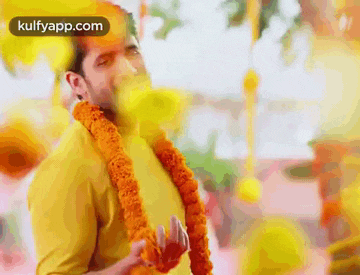 a man wearing a yellow shirt and a flower garland around his neck is making a funny face .