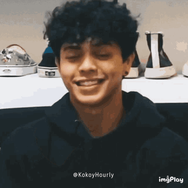 a young man with curly hair is smiling in front of a shelf with shoes on it