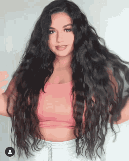 a woman with very long dark hair is wearing a pink crop top