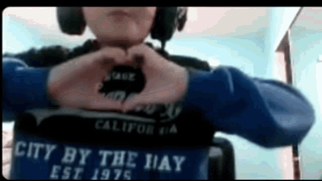 a person wearing headphones is making a heart shape with their hands