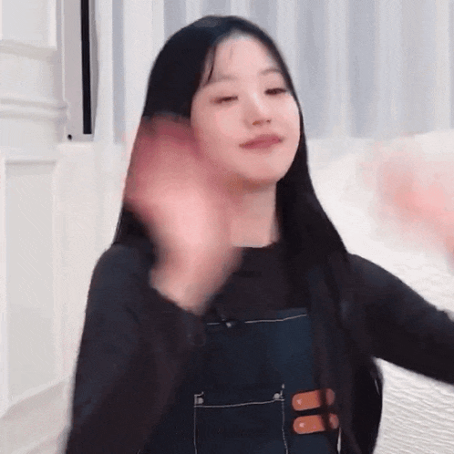 a woman with long black hair is waving at the camera .