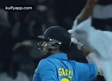 a cricket player wearing a helmet and a blue shirt with the name gandhi on the back .