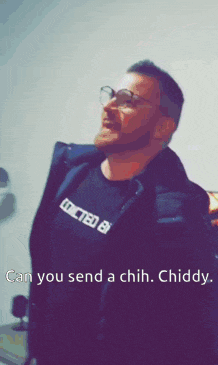 a man wearing glasses and a black shirt with the words " can you send a chih chuddy " on it