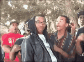 a group of people are dancing in a park and one of them is wearing a hooded jacket .