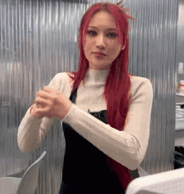 a woman with red hair is standing in front of a metal wall and holding her hands together .