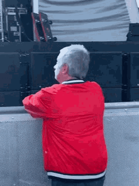 an elderly man in a red jacket is standing in front of a stage at a concert .
