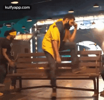 a man is sitting on a wooden bench while another man stands behind him .