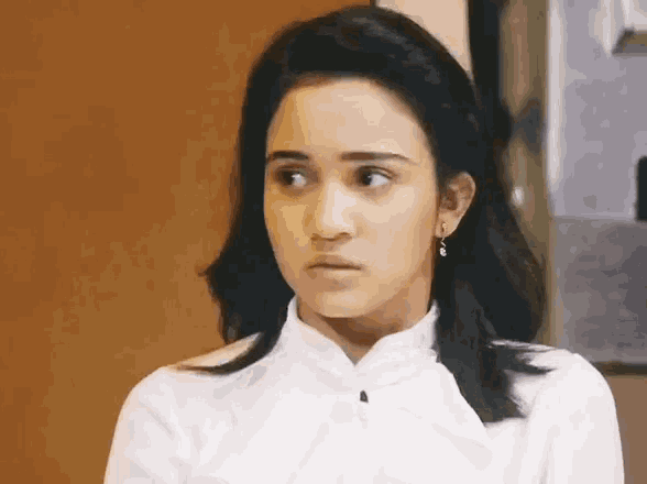 a woman wearing a white shirt and earrings is making a serious face