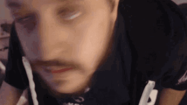 a man with a mustache is wearing a black shirt with the letter b on it