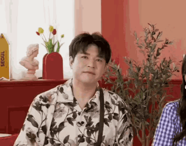 a man in a floral shirt is sitting next to a woman in a plaid shirt in a room .