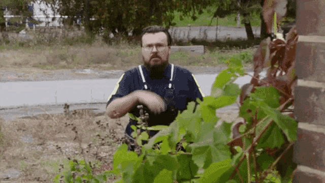 a man with a beard and glasses is standing in front of a plant .