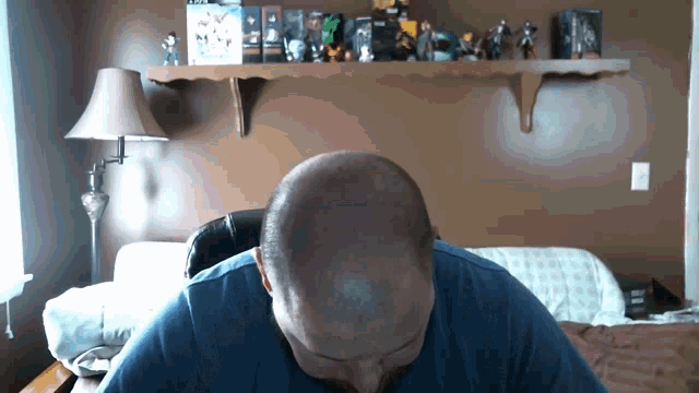a man with a shaved head is sitting in front of a shelf full of action figures