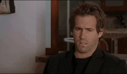 a man in a black suit is making a funny face while sitting in a kitchen .