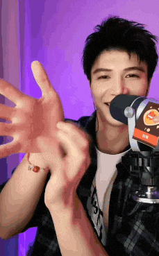 a man in a plaid shirt is standing in front of a microphone and making a heart shape with his hands